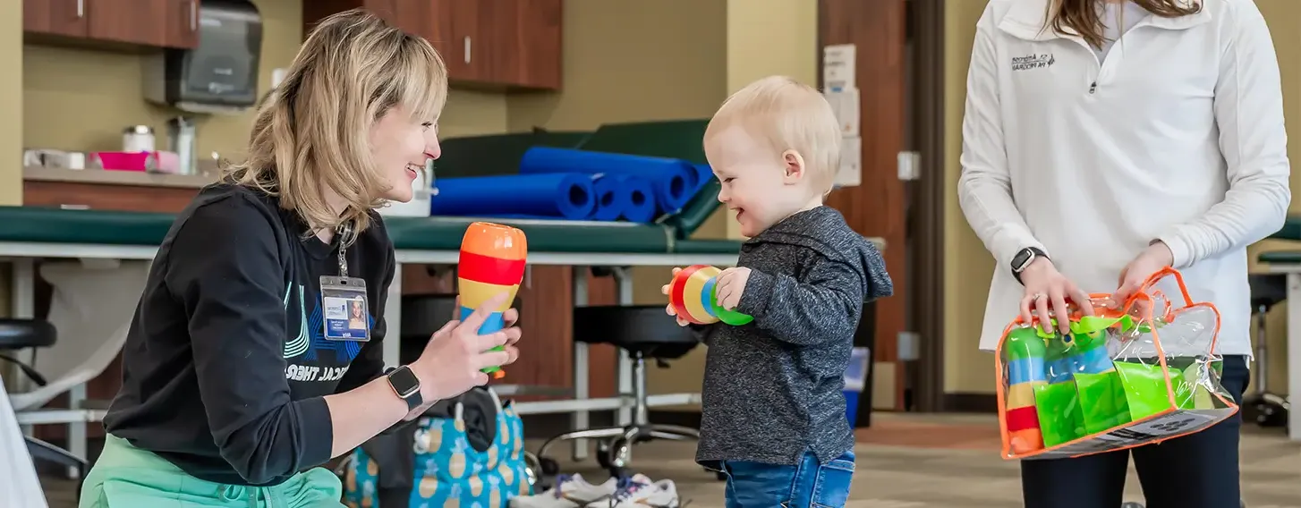 A woman conducting a pediatric assessment on the floor with a toddler.